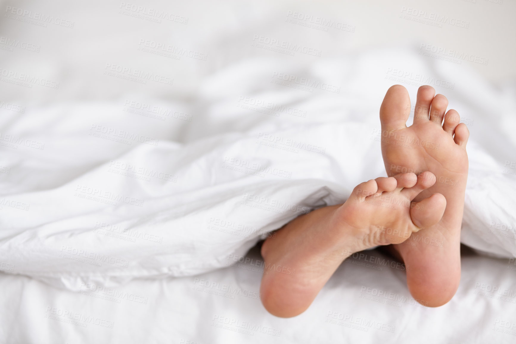 Buy stock photo Shot of a pair of woman's feet poking out from under the sheets of a bed
