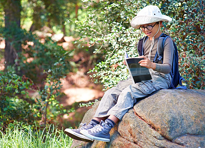 Buy stock photo A little boy with a book in his hand sitting on a rock