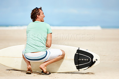Buy stock photo A young surfer crouched on the beach and looking away at the waves