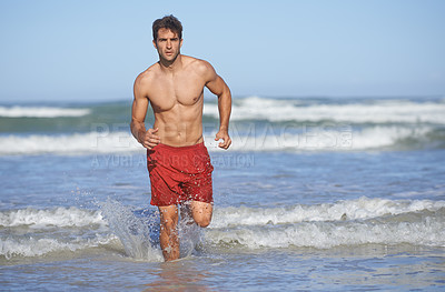 Buy stock photo A handsome young lifeguard running out from the sea