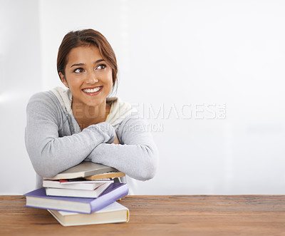 Buy stock photo Shot of a beautiful college student leaning on her books at her desk and looking thoughtful