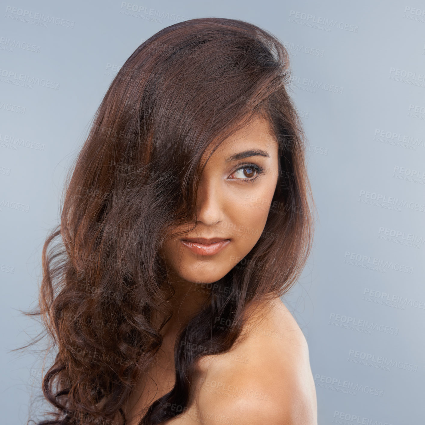 Buy stock photo Face, beauty and hair with wavy indian woman in studio on gray background for aesthetic wellness. Salon, spa or hairdresser with confident young model looking confident in natural haircare routine