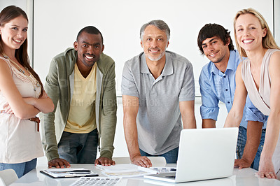 Buy stock photo A group of businesspeople standing behind a desk with a laptop on it smiling at the camera
