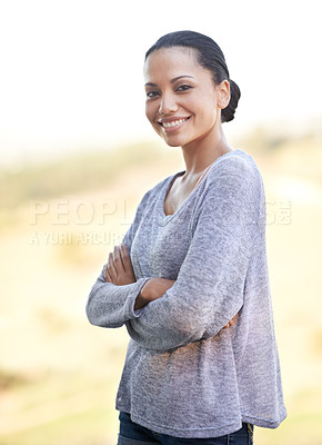 Buy stock photo Portrait of a confident young woman standing with her arms folded outdoors