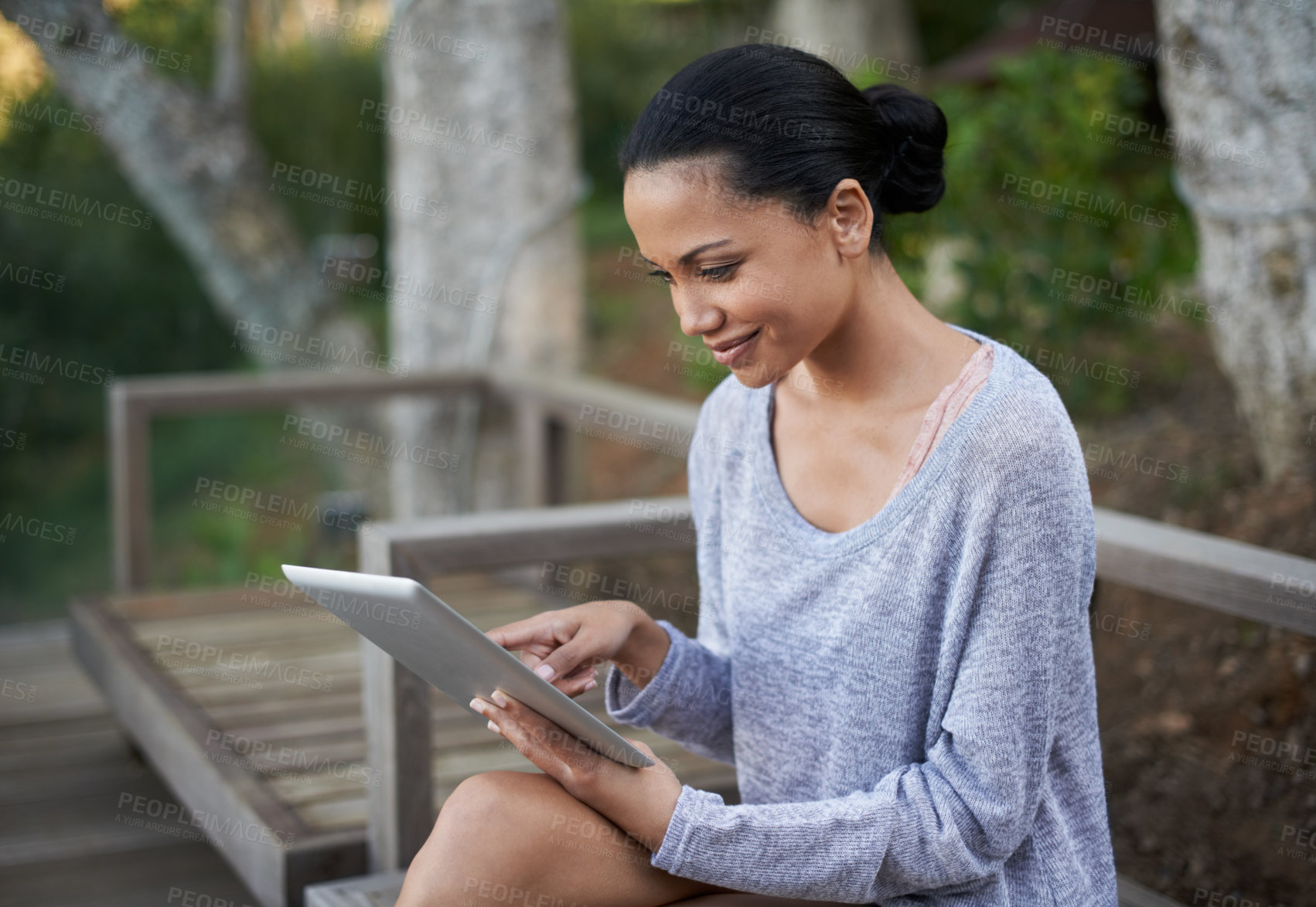 Buy stock photo Shot of an attractive young woman sitting on a park bench and working on a digital tablet outside