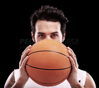 Buy stock photo A young man holding a basketball against a black background and looking at the camera