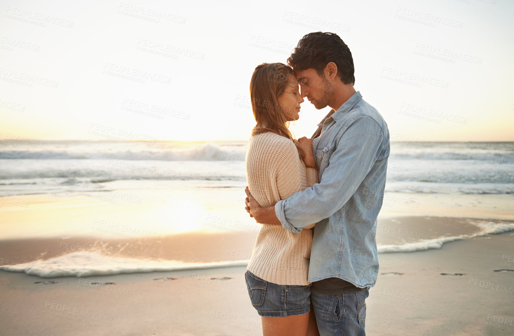 Buy stock photo A blissful young couple celebrating their love at sunset on the be