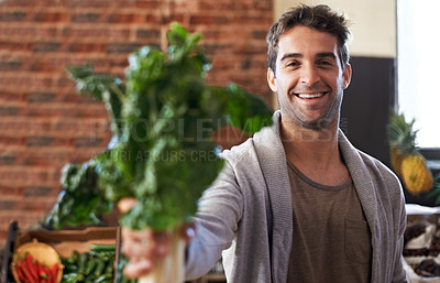 Buy stock photo Portrait of a young man in a grocery store holding up spinach to the camera