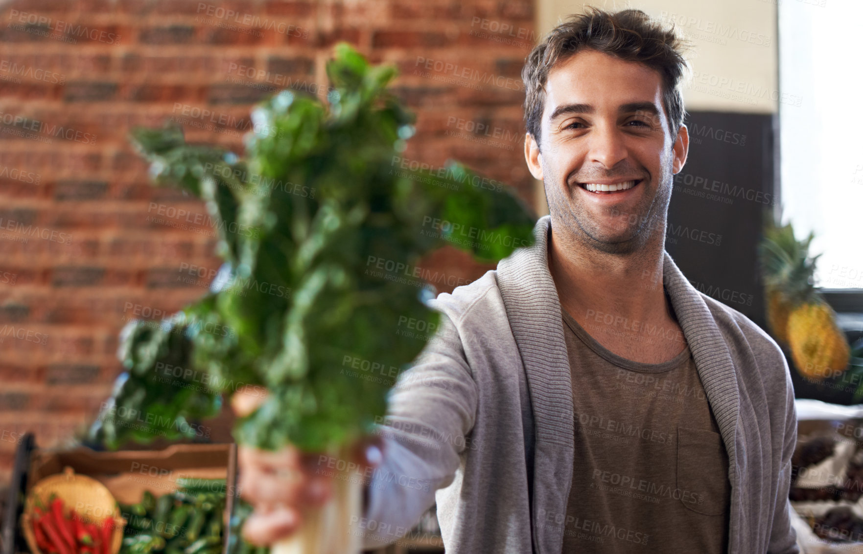 Buy stock photo Portrait of a young man in a grocery store holding up spinach to the camera