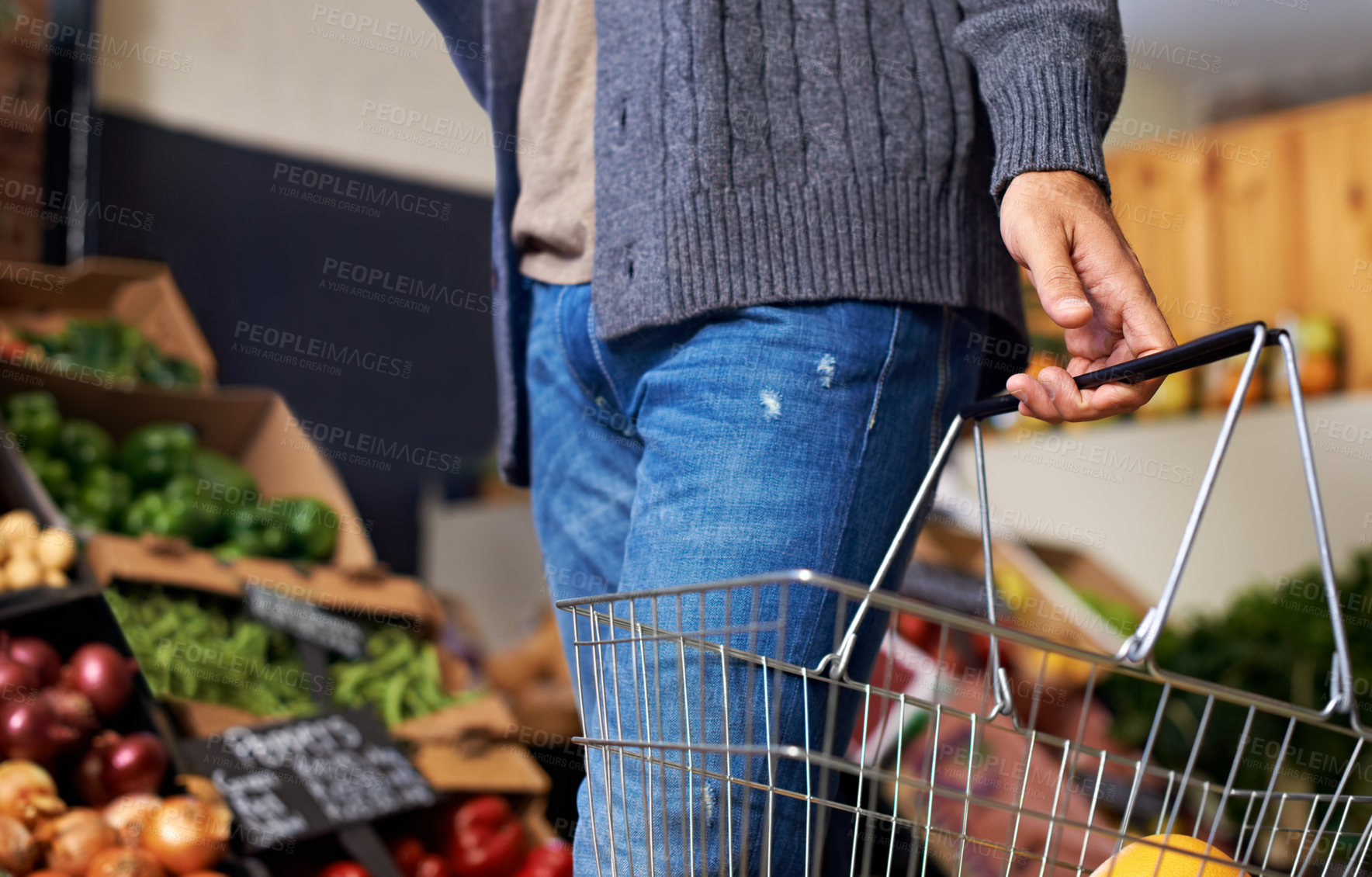 Buy stock photo Cropped shot of a young man walking down a grocery store aisle and carrying a basket with food in it