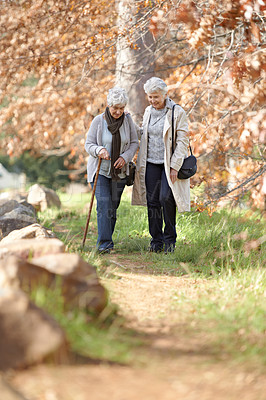 Buy stock photo Senior women, walking and support in park by autumn leaves, together and bonding on retirement in outdoor. Elderly friends, love and person with disability on vacation, care and talking in nature