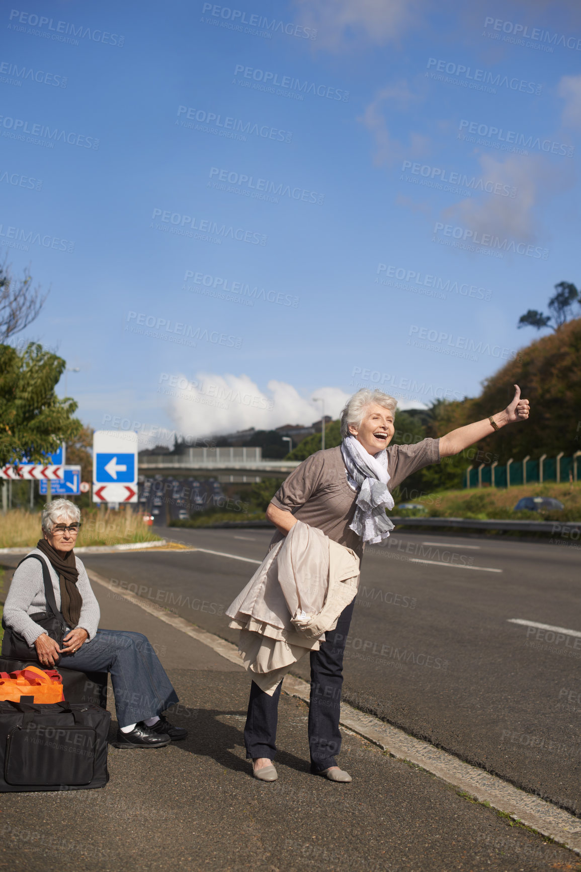 Buy stock photo Women, road and hitch hiker for travel in retirement, lift and friends in city with bags for adventure. Senior ladies, thumbs up and happy by roadside with hand gesture and stop transport to commute