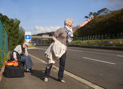Buy stock photo Travel, highway and senior friends hitchhiking together for adventure, escape or journey in retirement. Road, smile or happy and hand gesture with elderly women on sidewalk for holiday or vacation