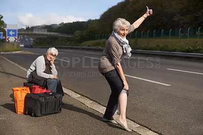 Buy stock photo Women, road and funny hitch hiker for travel in retirement, lift and senior friends in city with bags for adventure. Elderly, thumbs up and tired by roadside with comic and stop transport to commute