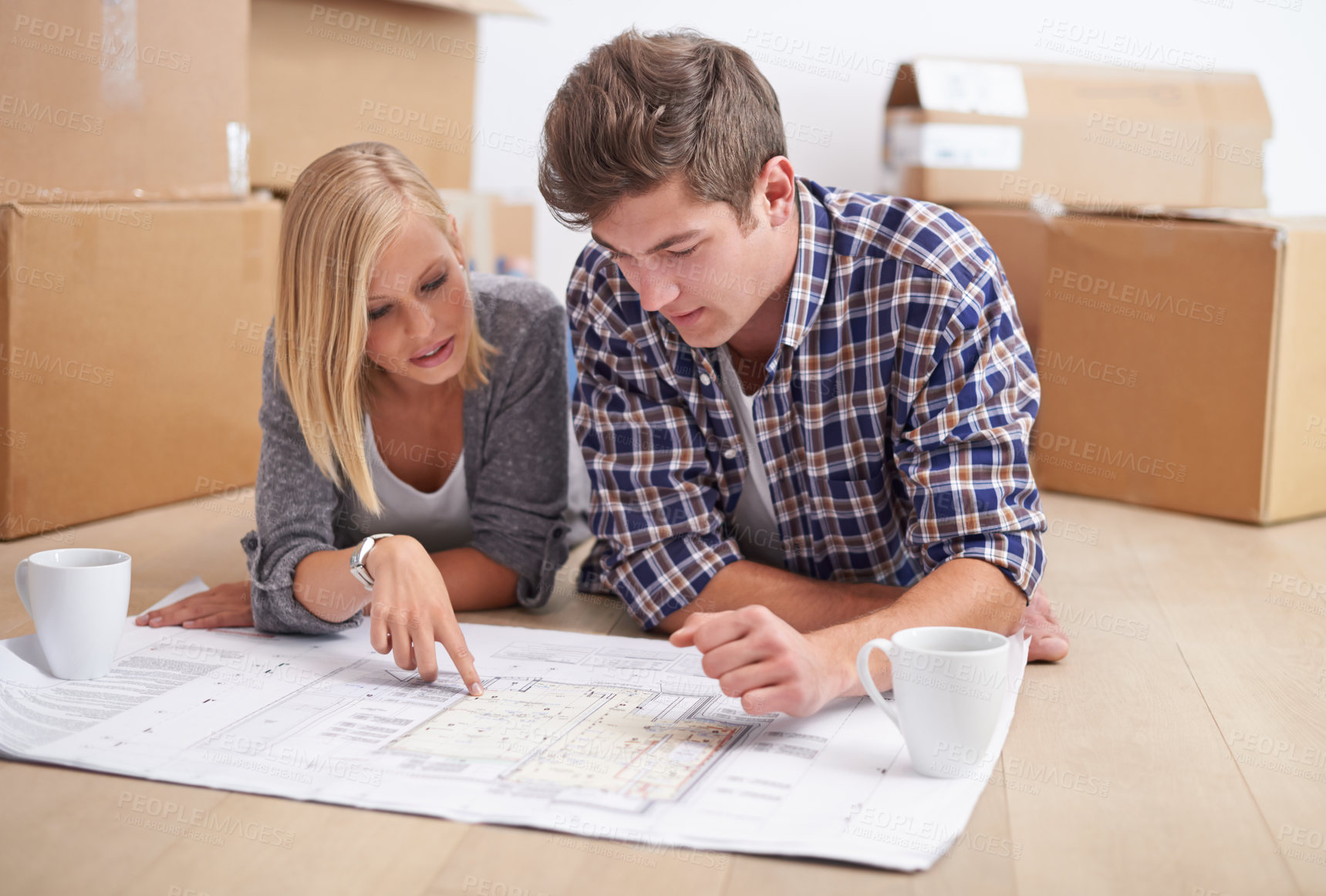 Buy stock photo A young couple lying on the floor with the blueprints of their new flat and boxes behind them