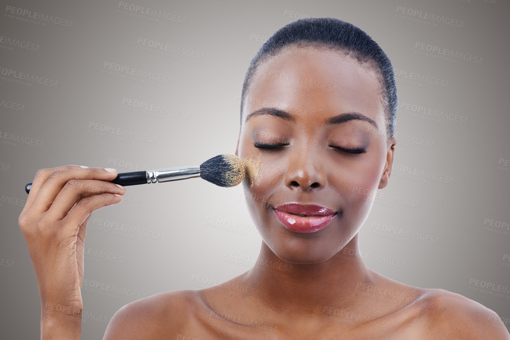 Buy stock photo Face, beauty and makeup brush with young black woman in studio on gray background to apply blush to cheek. Aesthetic, product and foundation with confident model using luxury cosmetics for makeover