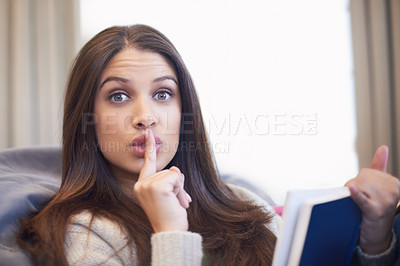 Buy stock photo Portrait of a young woman shushing the camera while reading a book