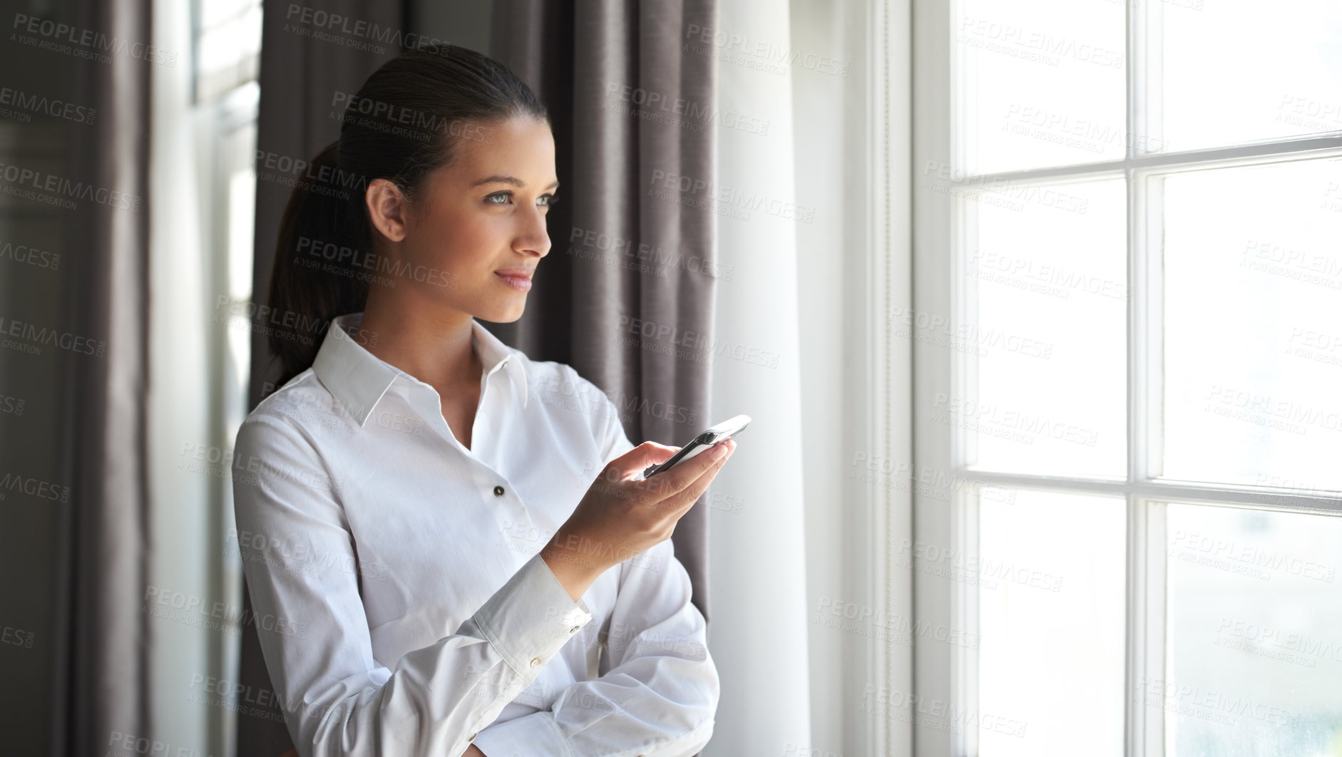 Buy stock photo Shot of a young businesswoman holding a cellphone near a window