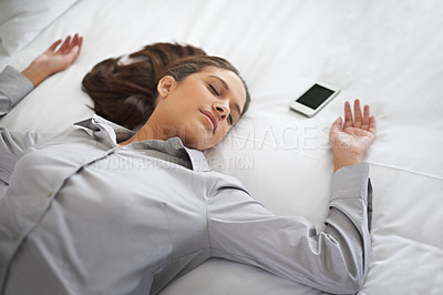 Buy stock photo Shot of a young businesswoman passed out on a bed with her cellphone beside here