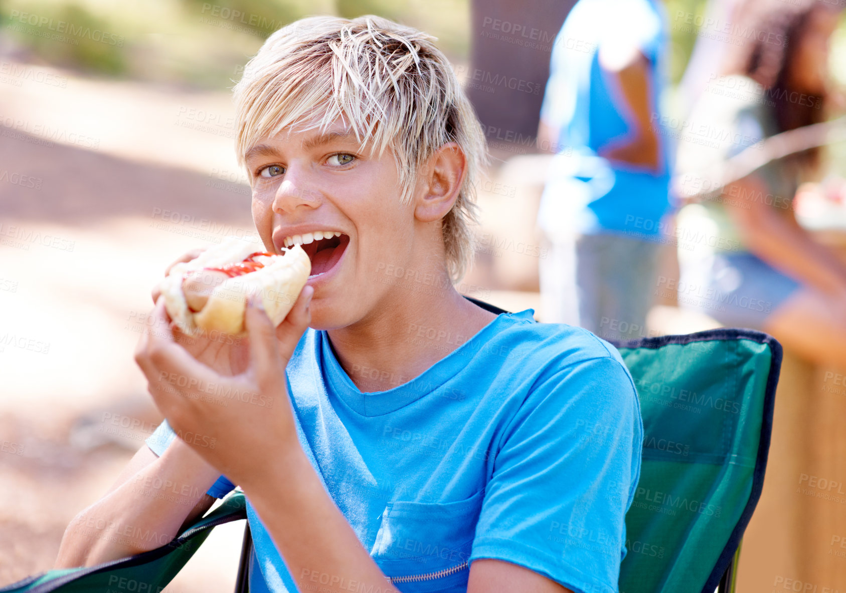 Buy stock photo A cute little boy eating a hot dog while outdoors
