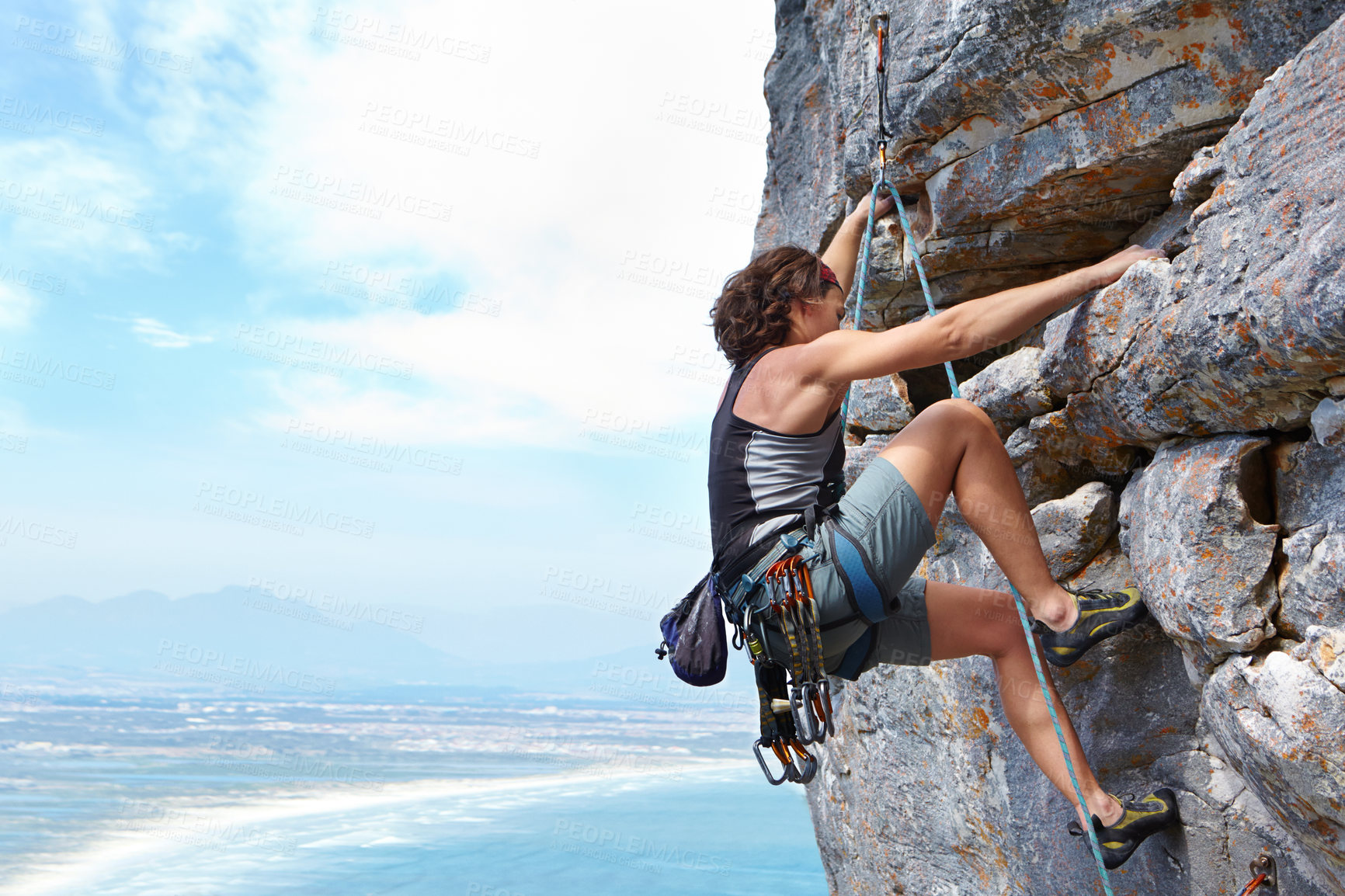 Buy stock photo A young woman climbing up a rock face while framed against a blue sky