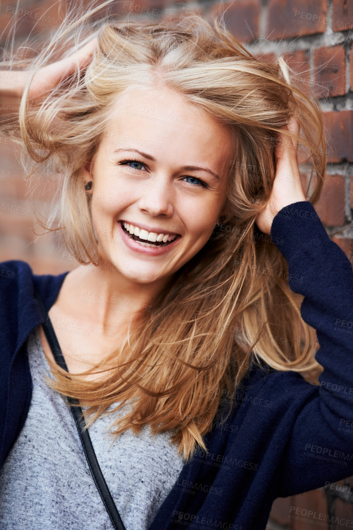 Buy stock photo Portrait, happy and woman with wind in hair by brick wall in city, funny or laugh outdoor. Face, fashion and smile of person, stylish casual clothes and blonde girl with breeze in Switzerland