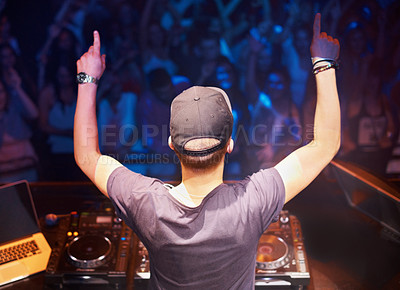Buy stock photo Rear view of a dj standing behind the decks with his hands in the air