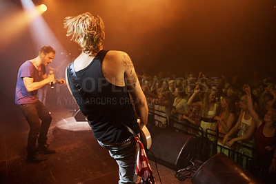 Buy stock photo Rock, concert and fans at stage with band in performance with singer and guitarist. Music festival, crowd and people with talent playing for audience in theater at night with spotlight and energy