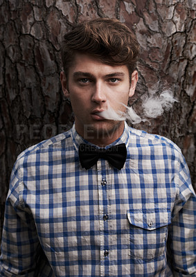 Buy stock photo Portrait of a young hipster smoking in front of a tree