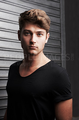 Buy stock photo Portrait of a handsome young man standing in front of some metal shutters