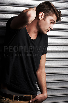 Buy stock photo Waist up shot of a handsome young man running his hands through his hair in front of some metal shutters