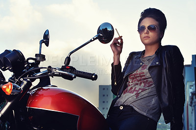 Buy stock photo Shot of a young female biker smoking a cigarette