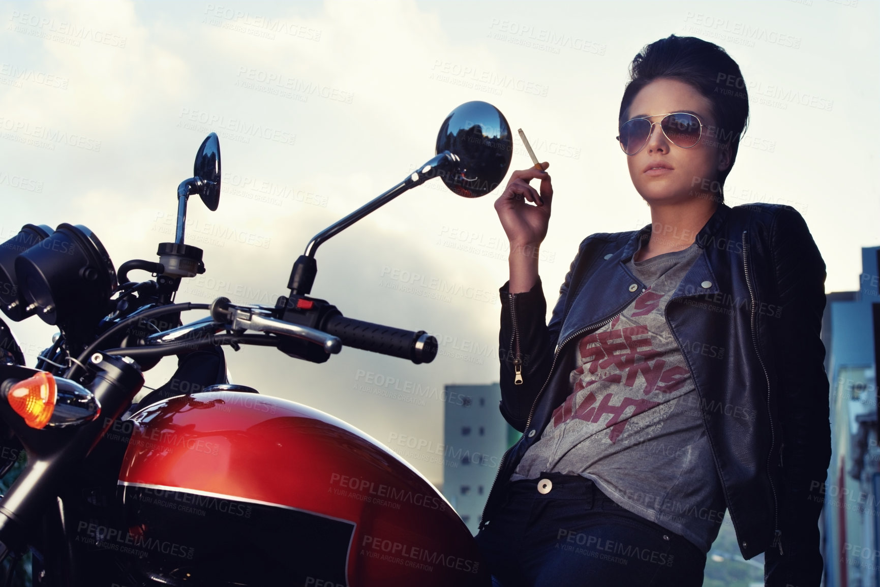 Buy stock photo Shot of a young female biker smoking a cigarette