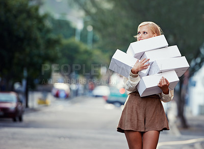 Buy stock photo A pretty young blond woman carrying a pile of clothing boxes on a downtown street