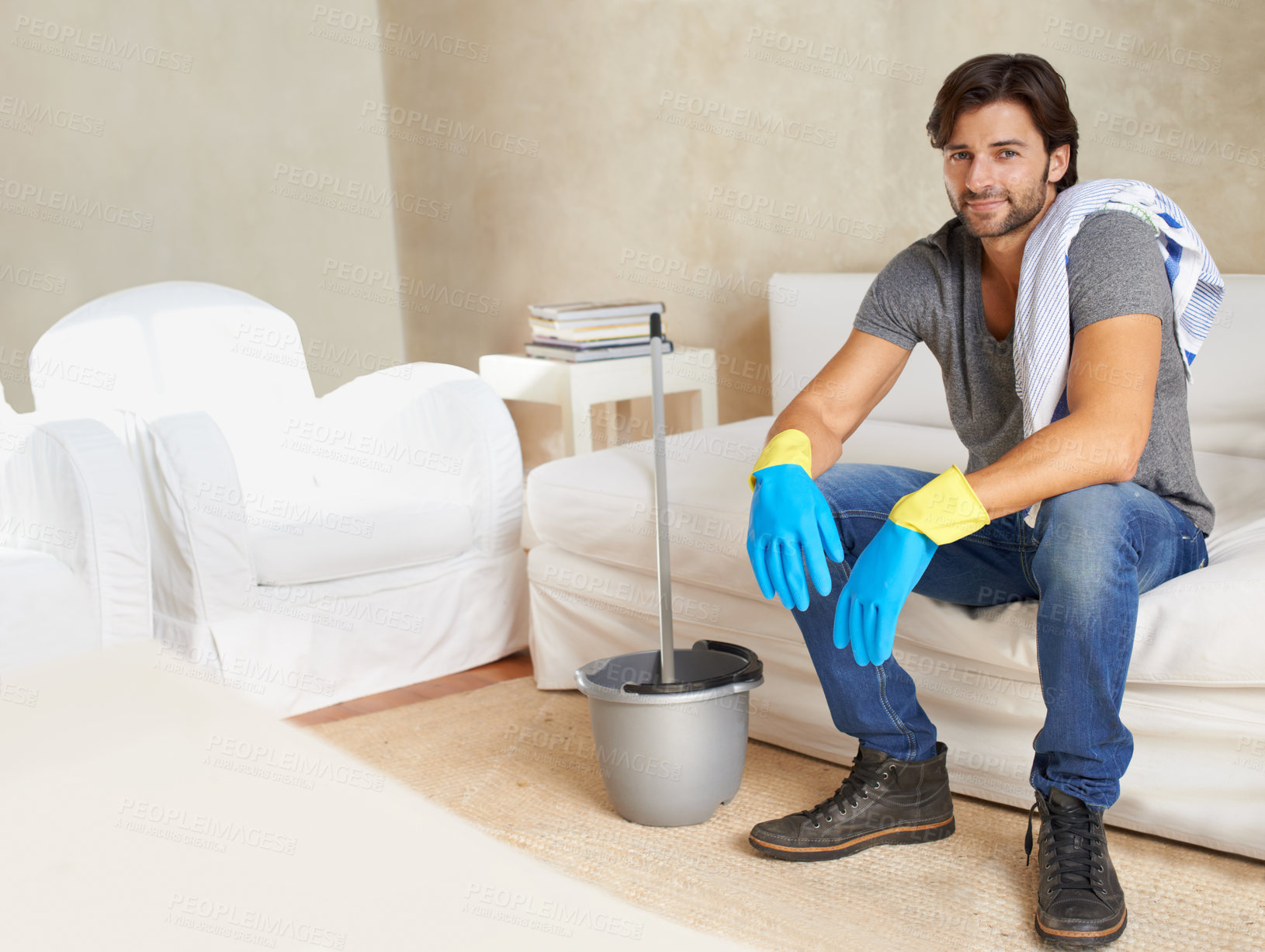 Buy stock photo Man, resting and sofa after cleaning house with mop, gloves or bucket during morning in Colombia. Professional cleaner, male domestic or char with tired smile in modern home for mockup or portrait