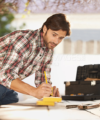 Buy stock photo A handsome young carpenter taking measurements of some wood