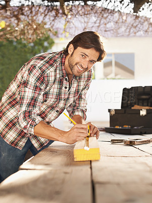 Buy stock photo A handsome young carpenter taking measurements of some wood