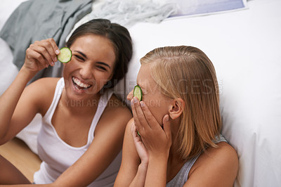 Buy stock photo Women, laughing and facial treatment with cucumber for wellness, wellbeing and selfcare at home. Female friends, fun and sitting near bed for bonding, skincare or rest and relaxation during sleepover