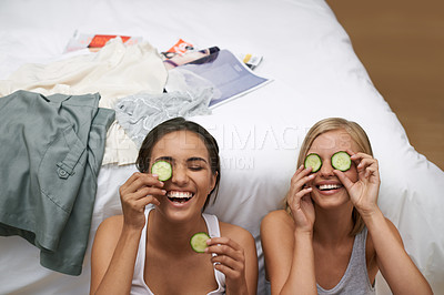 Buy stock photo Girl friends, laughing and facial treatment with cucumber for wellness, wellbeing and self care at home. Women, fun and sitting near bed for bonding, skincare or rest and relaxation during sleepover