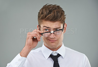 Buy stock photo A young man looking skeptically over his spectacles