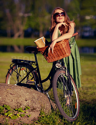 Buy stock photo Shot of a beautiful young woman relaxing in the park next to her old fashioned bicycle