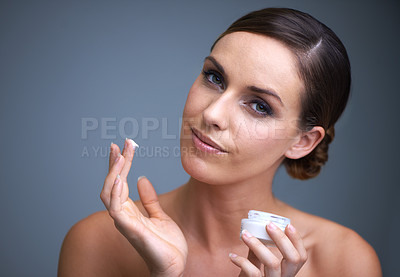 Buy stock photo Portrait of an attractive young woman applying moisturizer to her skin