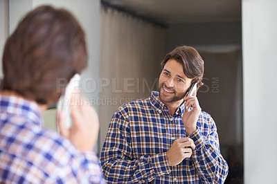 Buy stock photo Shot of a handsome man talking on the phone while getting ready for work