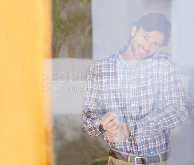 Buy stock photo Through the glass shot of a handsome man getting dressed while talking on the phone