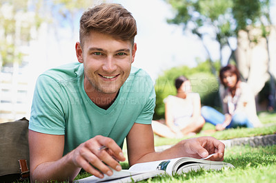 Buy stock photo A young man lying in the park studying