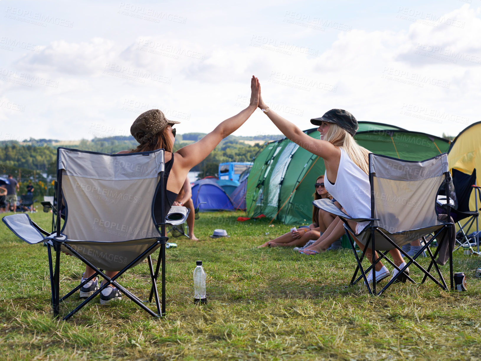 Buy stock photo Rearview shot of two friends giving each other a high five at an outdoor festival