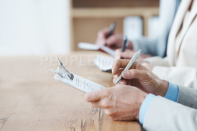 Buy stock photo Cropped shot of three coworkers sitting at a table and taking notes