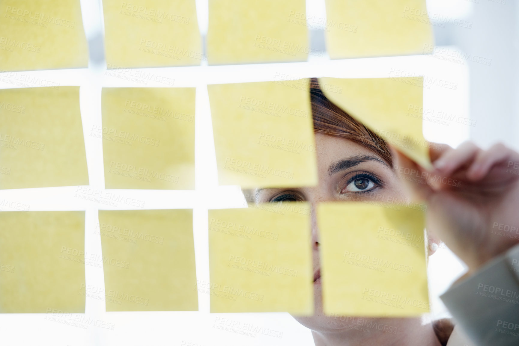 Buy stock photo Shot of a businesswoman arranging sticky notes on a glass wal