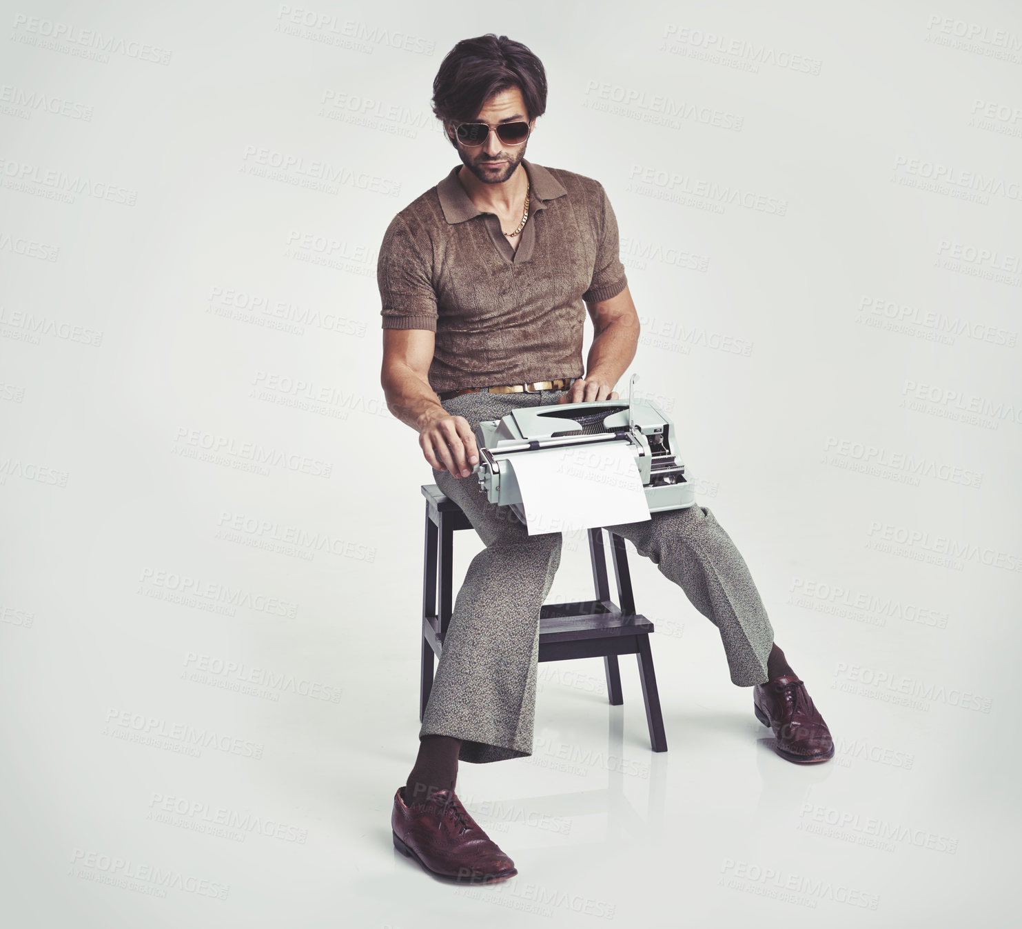 Buy stock photo A handsome man holding a retro typewriter and smoking a pipe while sitting  on a stool