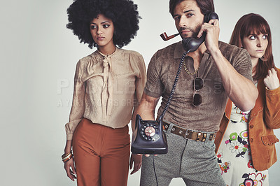 Buy stock photo Two attractive young hippies standing behind a handsome man using a retro telephone